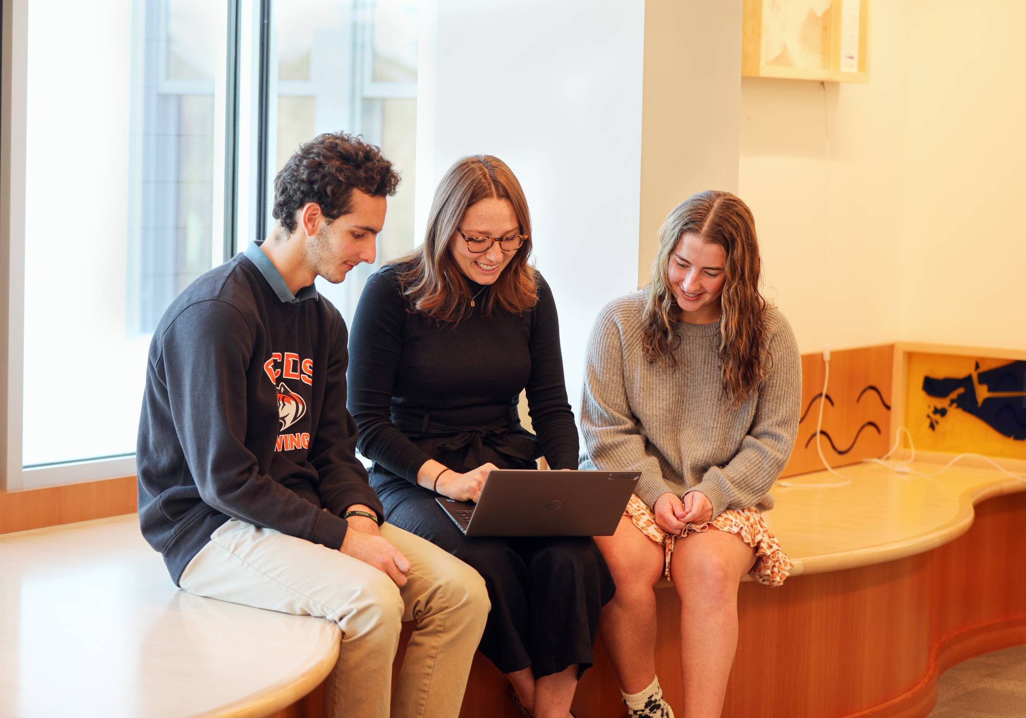 Photo of students sat together with a laptop outside of class